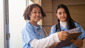 Zwei Frauen in medizinischer Arbeitskleidung lachen in die Kamera