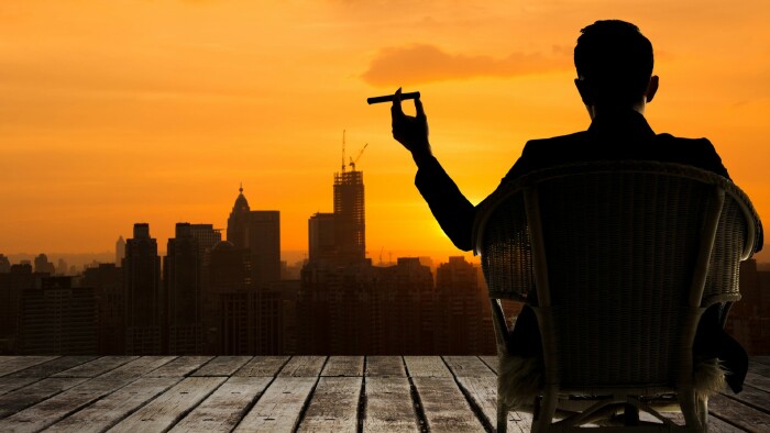  Silhouette eines Gesch&auml;ftsmannes, der auf einem Stuhl sitzt und eine Zigarre h&auml;lt und auf die Stadt blickt.