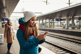 Frau wartet am Bahnsteig auf einen Zug und tippt etwas in ihr Handy