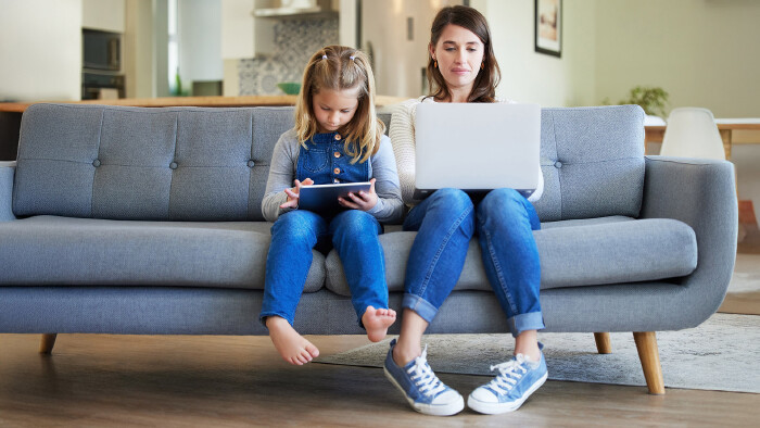 Mama mit Laptop und Kind mit Tablet sitzen auf dem Sofa.