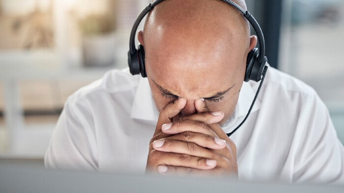 © peopleimages.com, stock.adobe.com Call Center Mitarbeiter mit Kopfschmerzen