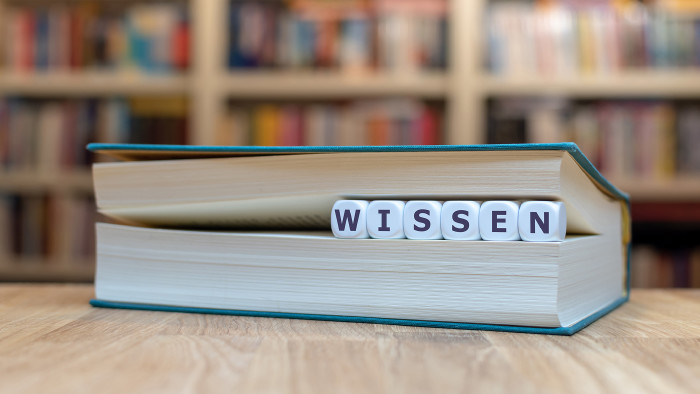 Würfel zwischen Buchseiten bilden das Wort Wissen.