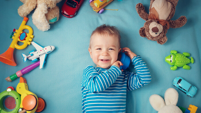 Glücklicher einjähriger Bub liegt mit vielen Plüschtieren auf einer blauen Decke
