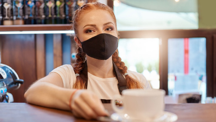 © sementsova321, stock.adobe.com Barista mit Mundschutz stellte eine Tasse Kaffee auf den Tresen © sementsova321, stock.adobe.com
