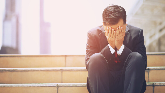 © methaphum, stock.adobe.com Junger Mann sitzt auf einer Stiege und ist verzweifelt.