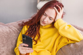 Frau sitzt auf der Couch und schaut ins Handy