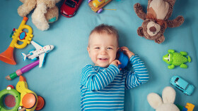 Glücklicher einjähriger Bub liegt mit vielen Plüschtieren auf einer blauen Decke