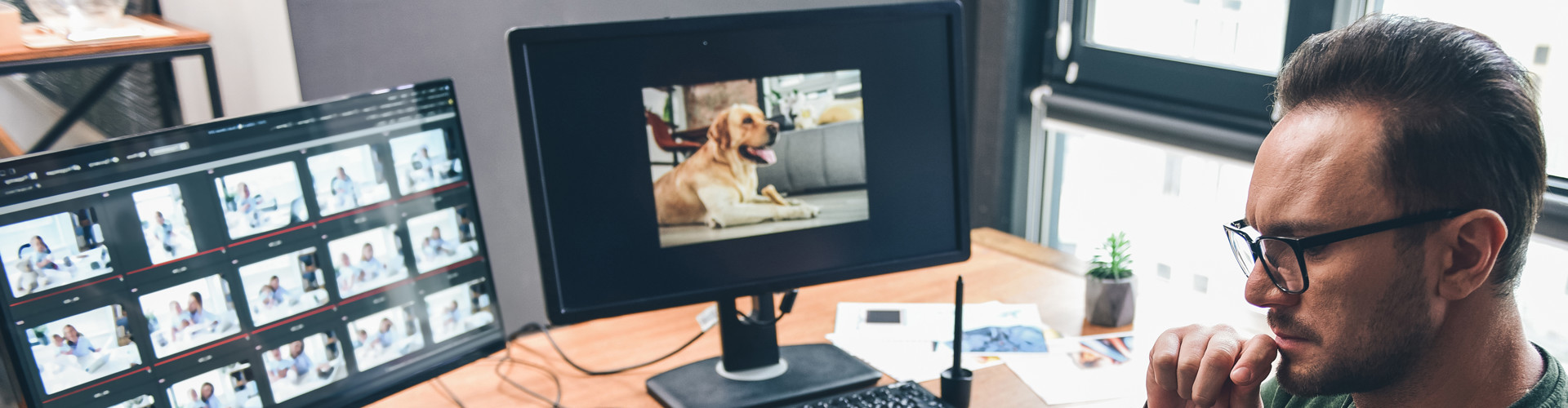 Junger Mann mit Brille sitzt am Schreibtisch, vor ihm stehen zwei Bildschirme © YakobchukOlena, stock.adobe.com