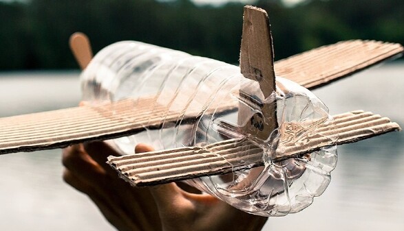 Kinderflugzeug aus einer PVC Flasche und Kartonflügeln gebastelt segelt über einen See