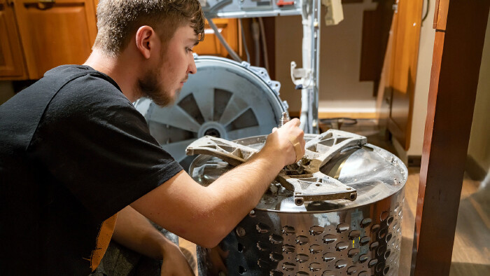 © denklim, stock.adobe.com Ein junger Mann repariert am Nachmittag eine Waschmaschine in einer Wohnküche