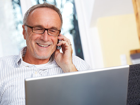 Mann mit Brille sitzt vor Laptop und telefoniert