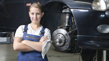 Automechanikerin steht stolz vor einem aufgebockten Fahrzeug © runzelkorn, stock.adobe.com