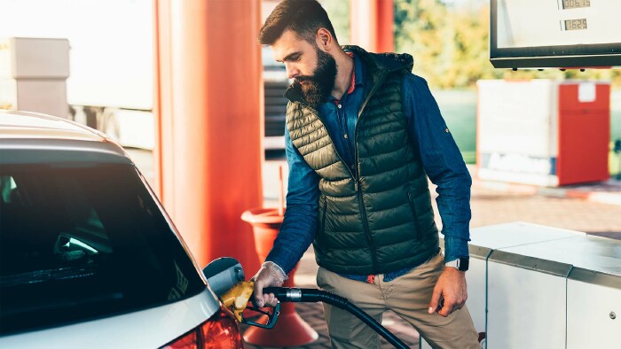 Junger, gutaussehender erwachsener Mann, der an der Tankstelle steht und sein Auto betankt.