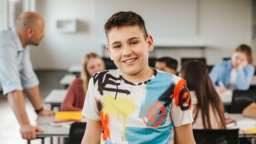 Schüler sitzt lächelnd in der Klasse und blickt in Richtung Kamera