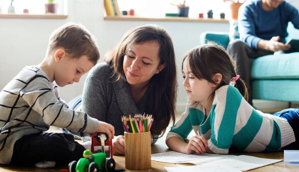 Mutter liegt mit Kindern am Boden und malt und spielt mit ihnen
