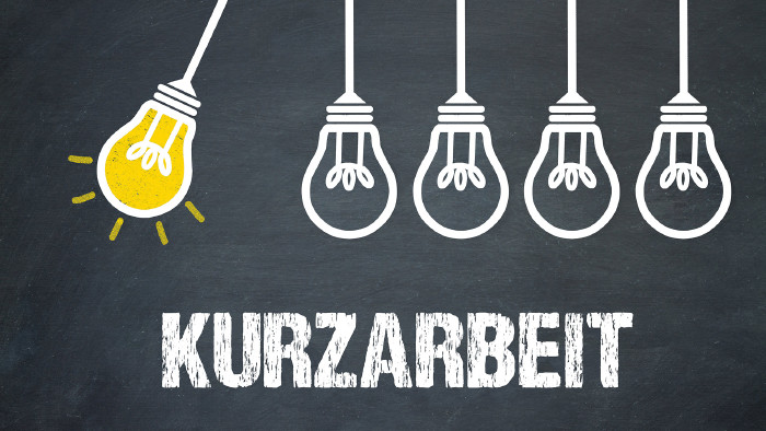 © magele-picture, stock.adobe.com Fünf Glühbirnen hängen über dem Schriftzug Kurzarbeit, eine davon schwingt und leuchtet © magele-picture, stock.adobe.com