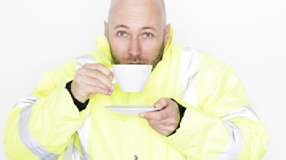 Ein Mann in Arbeitskleidung nippt an einer Tasse Tee, in der anderen Hand h&auml;lt er die Untertasse.