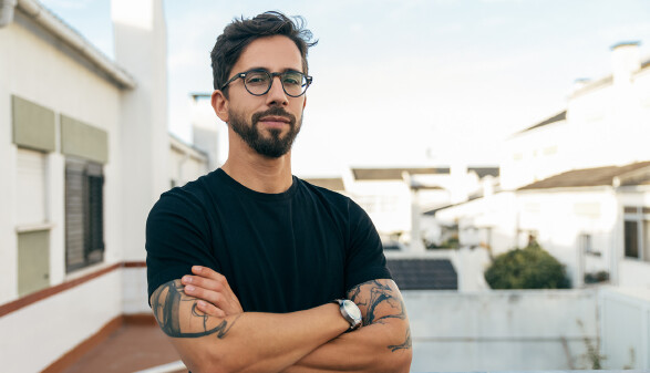 Junger Mann mit schwarzer Brille schaut mit verschränkten Armen in die Kamera © Mangostar, stock.adobe.com