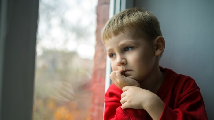 © luxorphoto, stock.adobe.com Kleiner Bub sitzt nachdenklich am Fenster