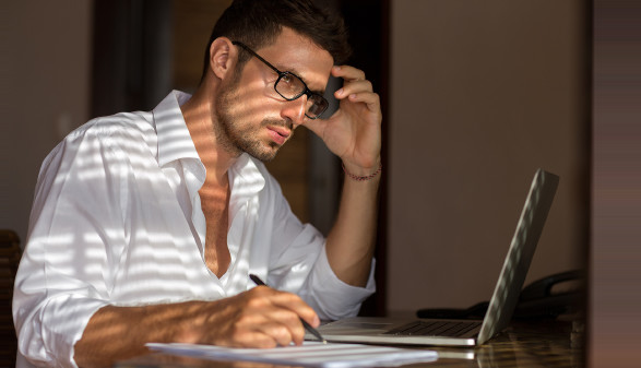 Mann mit Brille sitzt bei Notebook und &uuml;berlegt