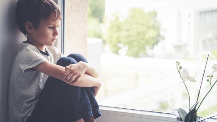 Trauriges Kind sitzt beim Fenster