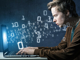 Junger Mann sitzt vor dem Laptop und tippt auf der Tastatur herum. Aus dem Bildschirm "schweben" ihm Zahlen entgegen.