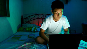 Jugendlicher mit Laptop auf dem Bett