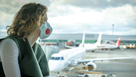 Frau mit Mundschutz blickt auf Flughafen © edojob , stock.adobe.com
