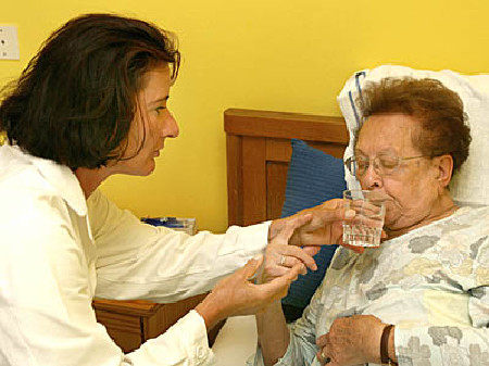 Pflegerin gibt der schwachen Pensionistin ein Glas Wasser.