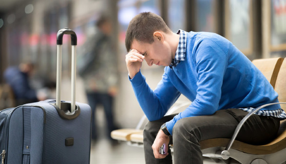 Urlauber sitzt mit Koffer nachdenklich am Flughafen