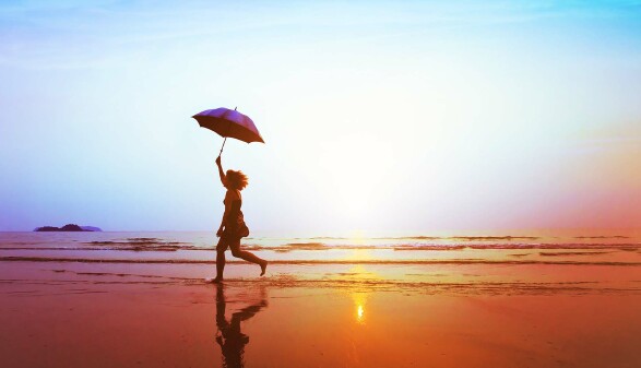 Silhouette eines glücklichen Mädchens mit Sonnenschirmsprung am Strand 