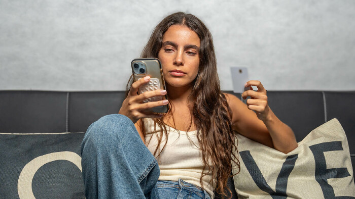 Frau sitzt auf Couch und t&auml;tigt &Uuml;berweisung mit Handy