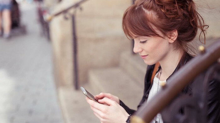 Junge Frau sitzt draußen auf einer Treppe und schaut auf ihr Handy