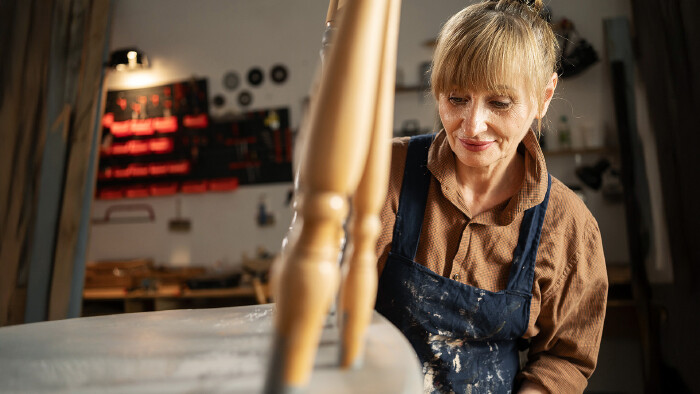 Eine ältere Tischlerin restauriert einen alten Stuhl.