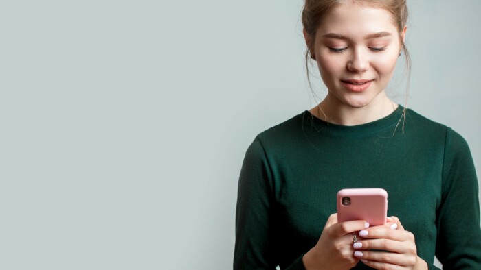 © alfa27, stock.adobe.com Nette junge Frau trägt ein grünes langärmeliges Hemd und hält ein Mobiltelefon in der Hand.