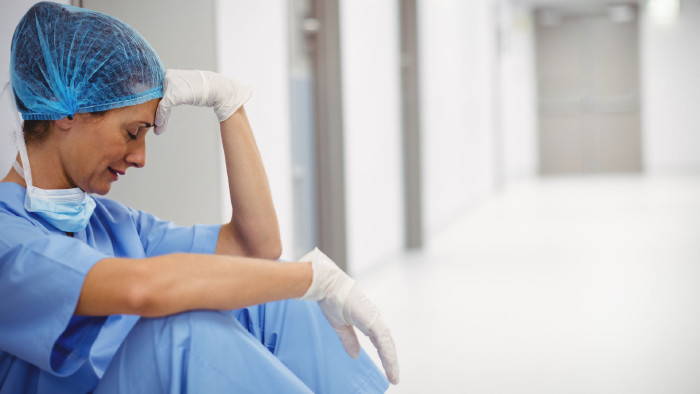 © WavebreakMediaMicro, Adobe Stock erschöpfte Pflegerin sitzt auf Krankenhausboden