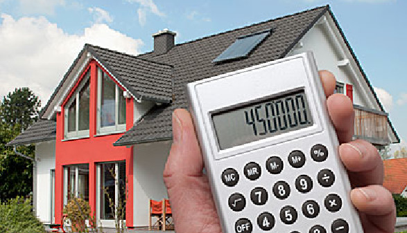 Haus im Hintergrund, Hand mit Taschenrechner im Vordergrund © Eisenhans_Fotolia.com, fotolia.com
