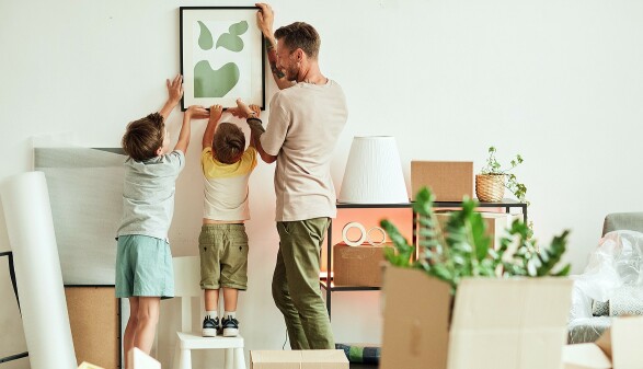 Papa und S&ouml;hne h&auml;ngen ein Bild in der neuen Wohnung auf